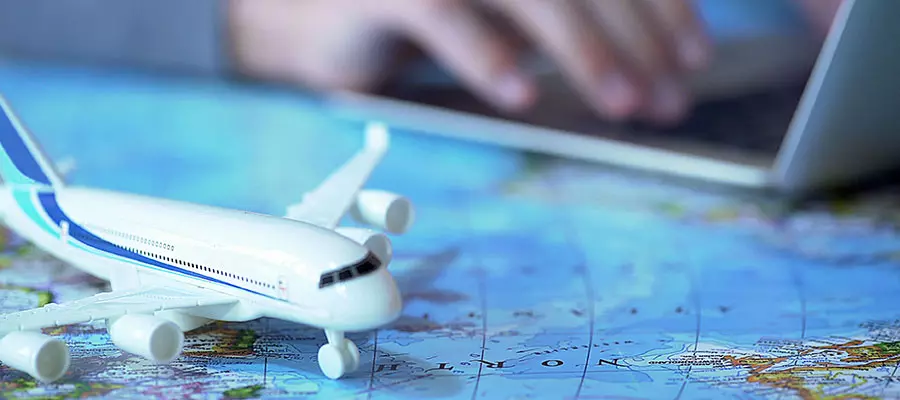 Avión en miniatura sobre una mesa, de fondo una persona usando una portátil.