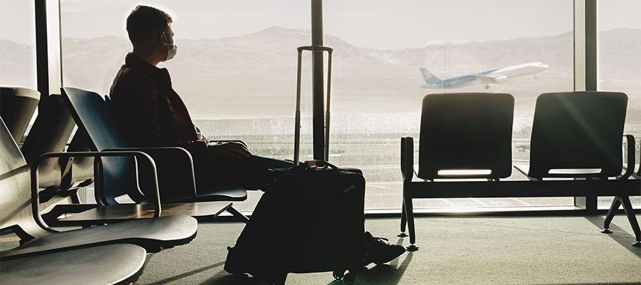 Hombre sentado en el aeropuerto con su maleta mirando a la pista de aterrizaje a través del ventanal.